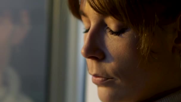 Close-up van een vrouw in een warme gebreide trui die in contemplatie uit het raam kijkt - Video