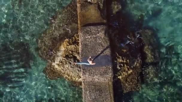 身体の上からスポーツウェア姿の女性が立ち上がる手と手と手ヨガポーズ岩の多い海岸で練習中 - 映像、動画