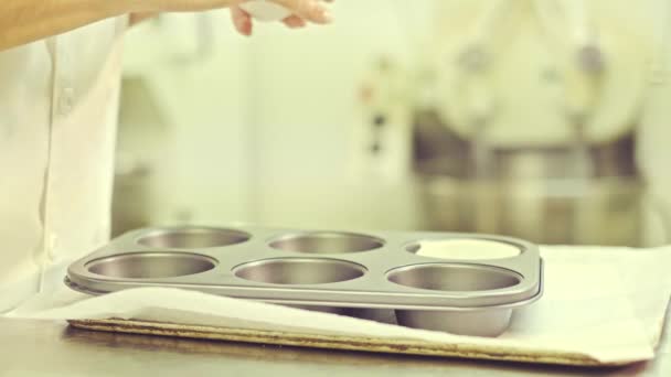 Boční pohled na anonymní cukrář aranžující papírové kelímky do kovového muffinového tácu před plněním těstem při přípravě pečiva v kuchyni - Záběry, video