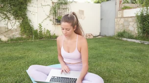 Klidná žena ve sportovním oblečení sedí bosá na podložce a vybírá online výuku pro cvičení jógy - Záběry, video