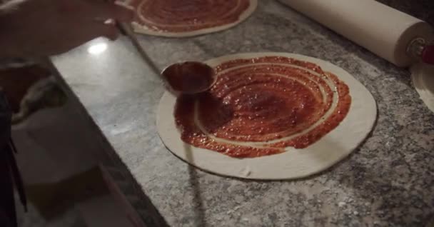 Chef anónimo recortado vertiendo y esparciendo salsa de tomate en la masa con cucharón mientras cocina pizza en la mesa en el restaurante - Metraje, vídeo