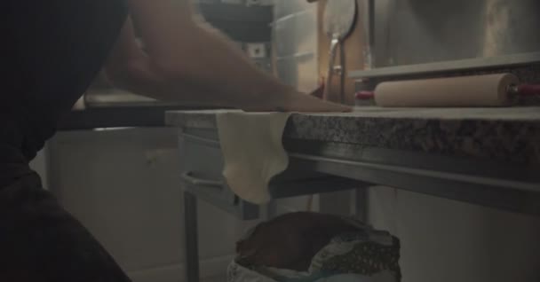 Crop male chef dusting table with flour and starting to stretch dough while cooking pizza in restaurant kitchen - Footage, Video