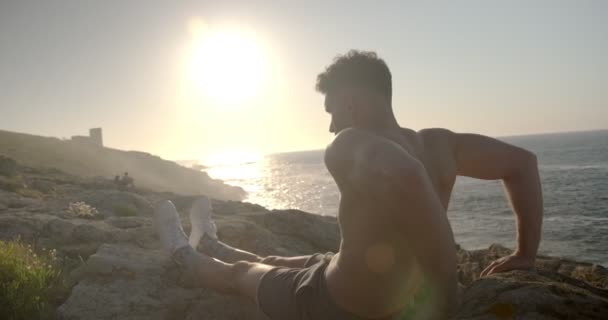 Vista posterior del entrenamiento de atleta masculino sin camisa enfocado en la orilla del mar y haciendo ejercicios de tríceps mientras mira hacia otro lado - Metraje, vídeo