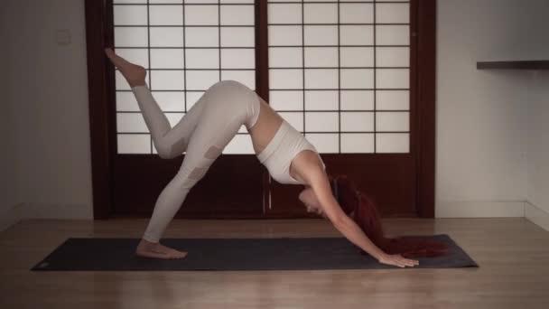 Mujer pelirroja joven haciendo yoga en la estera en casa - Imágenes, Vídeo