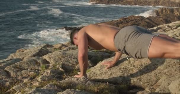 Πλευρική άποψη του εστιασμένου γυμνού ανδρικού αθλητή προπόνηση στην παραλία και να κάνει push-ups ασκήσεις - Πλάνα, βίντεο