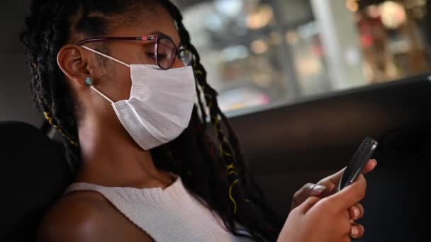 Mladý afro latina v obličeji maska procházející telefon na zadním sedadle auta - Záběry, video