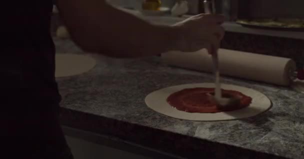 Chef anónimo recortado vertiendo y esparciendo salsa de tomate en la masa con cucharón mientras cocina pizza en la mesa en el restaurante - Metraje, vídeo