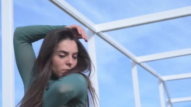 Χαμηλή γωνία της νεαρής ανεξάρτητης γυναικείας μπαλαρίνας που χορεύει ενάντια στη θολή γεωμετρική κατασκευή και τον γαλάζιο ουρανό - Πλάνα, βίντεο