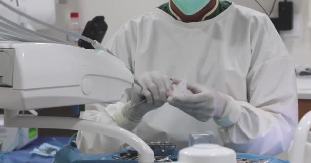 Professionale dentista in maschera e uniforme disimballaggio strumento dentale e paziente operatorio in clinica - Filmati, video