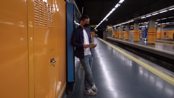 Αγνώριστος νεαρός άνδρας με μάσκα με βιβλίο αντιγράφων ετοιμάζεται για εξετάσεις κατά την άφιξη του μετρό κατά τη διάρκεια της πανδημίας COVID 19 - Πλάνα, βίντεο
