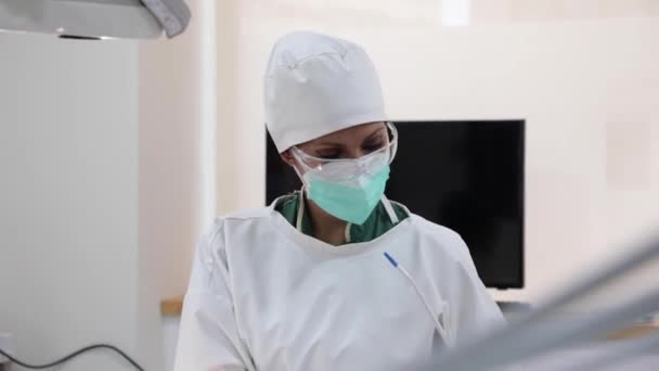 Dentisti in maschera e paziente operatorio uniforme sdraiato sulla sedia dentale in una moderna clinica luminosa - Filmati, video