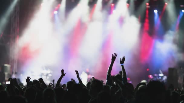 Achteraanzicht silhouetten van mensen met handen omhoog tegen verlicht met lichten podium tijdens muziekuitvoering - Video