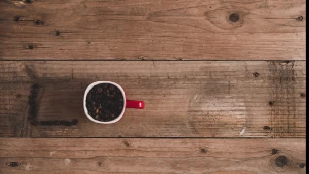 Top view stop motion animasyonu kırmızı fincanda kavrulmuş taze kahve çekirdeklerinin ahşap masada americano yazıtları oluşturması. - Video, Çekim