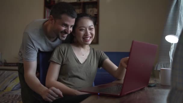 Felice fidanzato aiutare asiatico fidanzata working su il computer a casa - Filmati, video