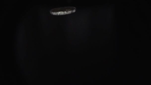 Monedas metálicas de primer plano girando en costilla en cámara lenta en habitación oscura sobre fondo negro - Metraje, vídeo