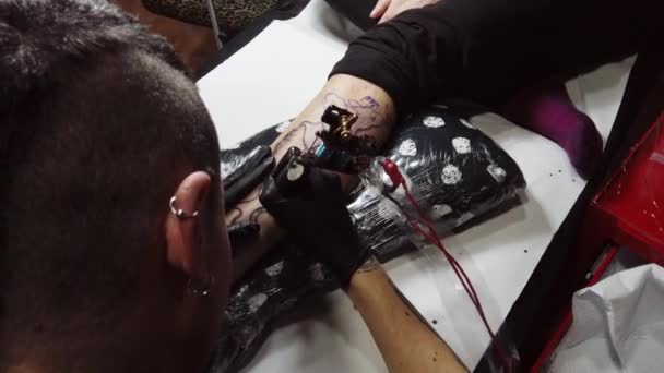 Мастер татуировки урожая делает контур на ноге клиента - Кадры, видео