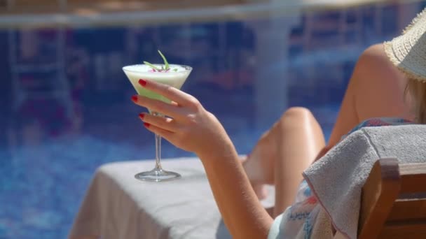Crop of unrecognizable female tourist drinking refreshing cocktail while sunbathing on deckchair near swimming pool - Video
