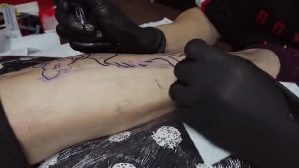 Cultivo tatuaje maestro haciendo contorno en la pierna del cliente - Imágenes, Vídeo