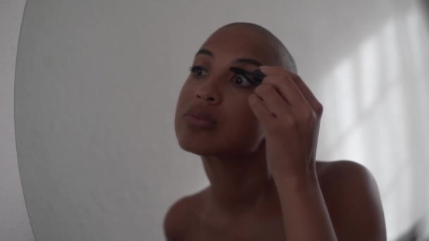 Αφροαμερικανή γυναίκα με φαλακρό κεφάλι κάνει μακιγιάζ και βάζοντας μαύρη μάσκαρα στις βλεφαρίδες - Πλάνα, βίντεο