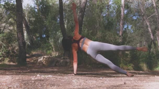 Zadní pohled na anonymní mladou ženu ve sportovním oblečení cvičící Vasisthasana bosá pro rozvoj rovnováhy a posilování svalů abs a paží v borovém lese - Záběry, video