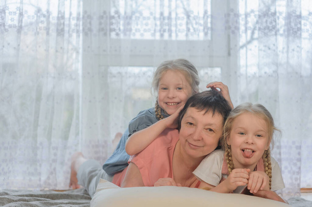 Portret rodzinny. Siostry wnuczki leżą na podłodze domu, patrzą w kamerę i uśmiechają się - Zdjęcie, obraz