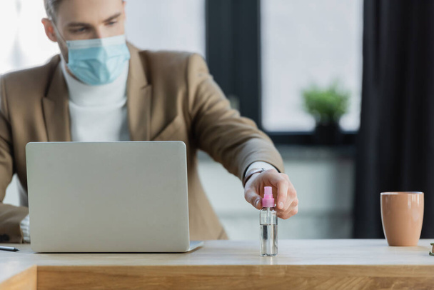 businessman in protective mask taking hand sanitizer, blurred background - Photo, Image