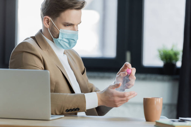hombre de negocios en máscara protectora aplicando desinfectante de manos en el lugar de trabajo - Foto, Imagen