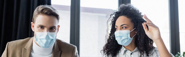 mujer de negocios afroamericana en gesto máscara médica mientras habla con colega, pancarta - Foto, imagen