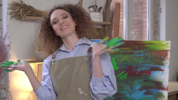 Retrato de una feliz artista moderna en un taller creativo. Un artista innovador pintó una pintura de abstracción con sus dedos - Metraje, vídeo
