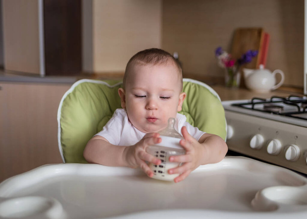 Niño sentado en una silla de alimentación y bebe de un biberón - Foto, imagen