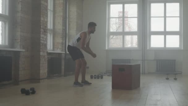 Plan complet au ralenti d'un sportif afro-américain qui s'étire un peu, puis commence à faire des sauts en boîte en faisant de l'entraînement d'endurance à l'intérieur dans un studio de gym fumé de style loft - Séquence, vidéo