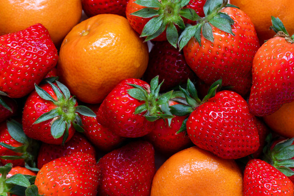 Agrumi freschi e intensamente colorati, clementine e fragole che possono essere utilizzati come sfondo perché include l'intera foto. - Foto, immagini