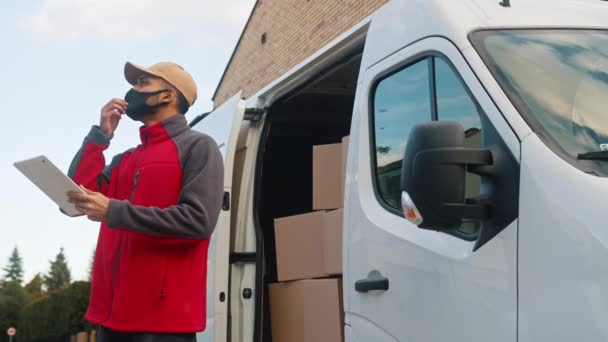 Giovanotto davanti al furgone di consegna che controlla il pacco del cliente con tablet digitale mentre indossa la maschera - Filmati, video
