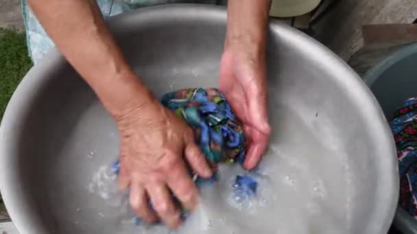 Las manos arrugadas envejecidas de la mujer mayor arrugan el textil azul mientras lava la ropa a mano - Imágenes, Vídeo