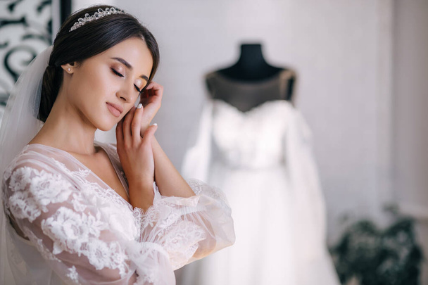 Morgen der Braut. Ein schönes Mädchen steht in einem weißen Gewand. Kleid mit Spitze auf einer Schaufensterpuppe - Foto, Bild