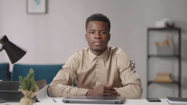 πορτρέτο ενός σοβαρού και ευγενικού νεαρού μαύρου άνδρα που κάθεται στο τραπέζι στο γραφείο του, αφροαμερικανού τύπου - Πλάνα, βίντεο