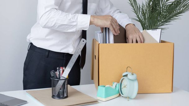 Ponga el equipo de trabajo en la oficina en una gran caja marrón, Los hombres de negocios están guardando documentos de trabajo y pertenencias personales debido a la renuncia o ser despedido, terminación del empleo. - Foto, imagen