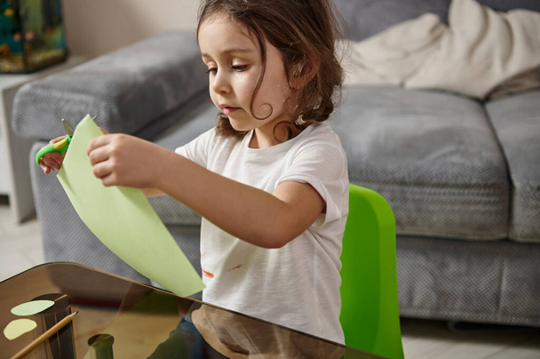 Petite fille préscolaire concentrée sur la coupe du papier couleur. - Photo, image