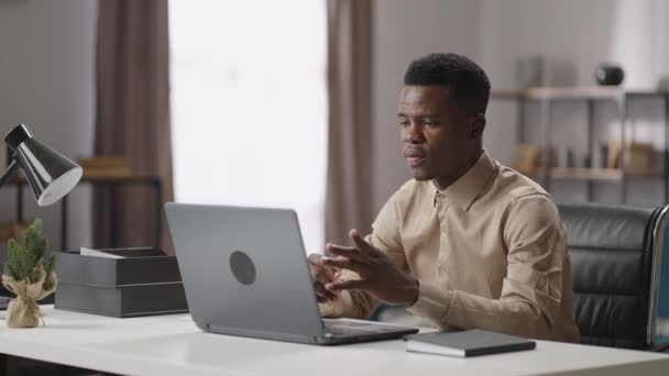 junger schwarzer Mann kommuniziert per Videochat im Laptop, arbeitet von zu Hause oder im Büro, mittleres Porträt drinnen - Filmmaterial, Video