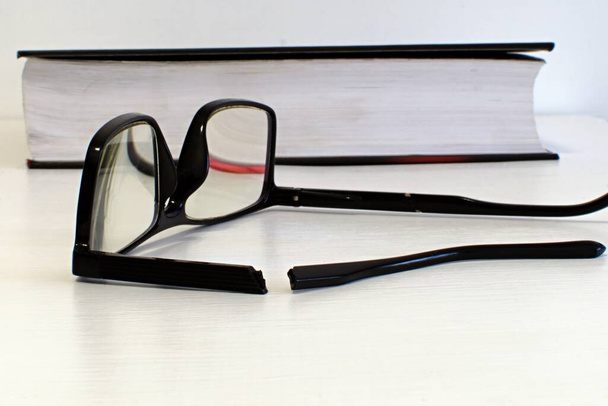 rozbité brýle na rozmazaném pozadí bílého stolu a otevřené knihy - Fotografie, Obrázek