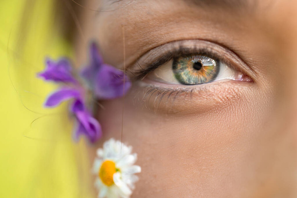 Makro strzał kobiet piękne oko i dzikie kwiaty na twarzy. skóry kobiet Pielęgnacja - Zdjęcie, obraz