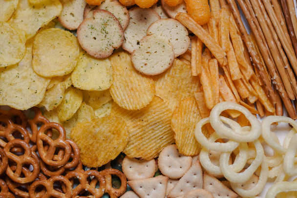Mnoho druhů nezdravých slaných svačinek: hranolky, sušenky, preclíky, cibulové kroužky. Horní pohled. Pozadí - Fotografie, Obrázek