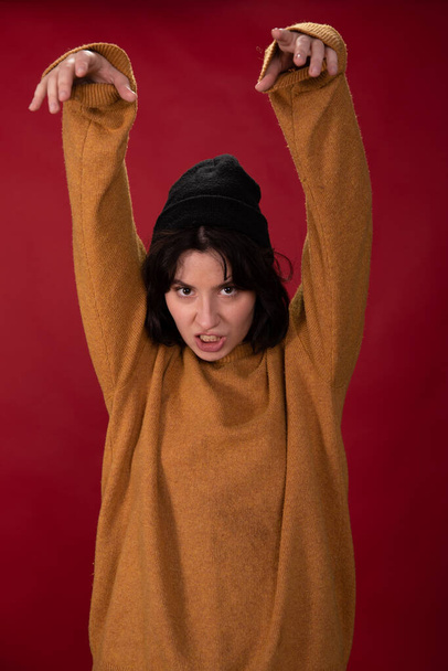 μελαχρινή hipster κορίτσι σε πουλόβερ μουστάρδα σηκώνοντας χέρι προσποιείται αρπακτικό - Φωτογραφία, εικόνα