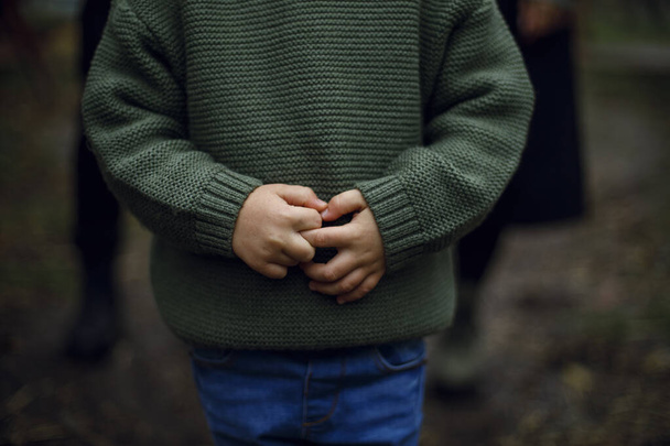 un petit garçon vêtu d'une veste chaude tient ses mains. peur et insécurité enfantines. gros plan et sans visage. Mains d'enfants - Photo, image