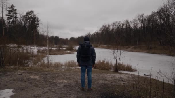 Eenzame droevige man, met zijn rug naar bevroren meer in het bos kijkend. Depressie, slecht humeur en zelfmoordgedachten. Ik heb psychologische hulp nodig. Winter natuur en mannelijk denken over het leven - Video