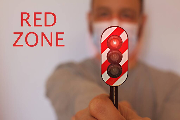 Homem com uma máscara cirúrgica segurando um semáforo com o sinal vermelho ligado, conceito de zona vermelha durante o Coronavirus - Foto, Imagem