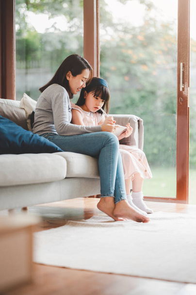 Feliz familia asiática madre e hija usando tableta digital para estudiar juntos en casa. - Foto, Imagen