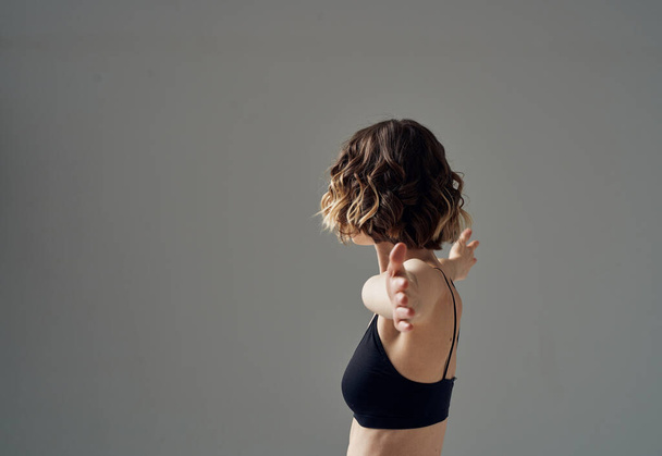 Una donna in una t-shirt corta su uno sfondo grigio gesti con le mani alle spalle nude Fitness Yoga asana - Foto, immagini