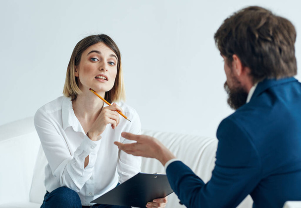Een man in een pak zit op een stoel en een vrouw op een bank psycholoog communiceren - Foto, afbeelding