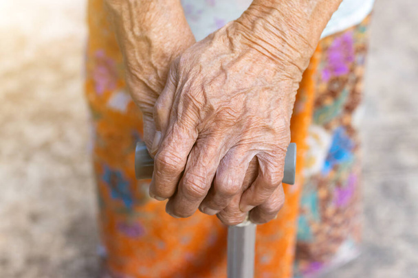 Азиатская старуха, стоящая с руками на трости, рука пожилой женщины, держащей посох для помощи в ходьбе - Фото, изображение